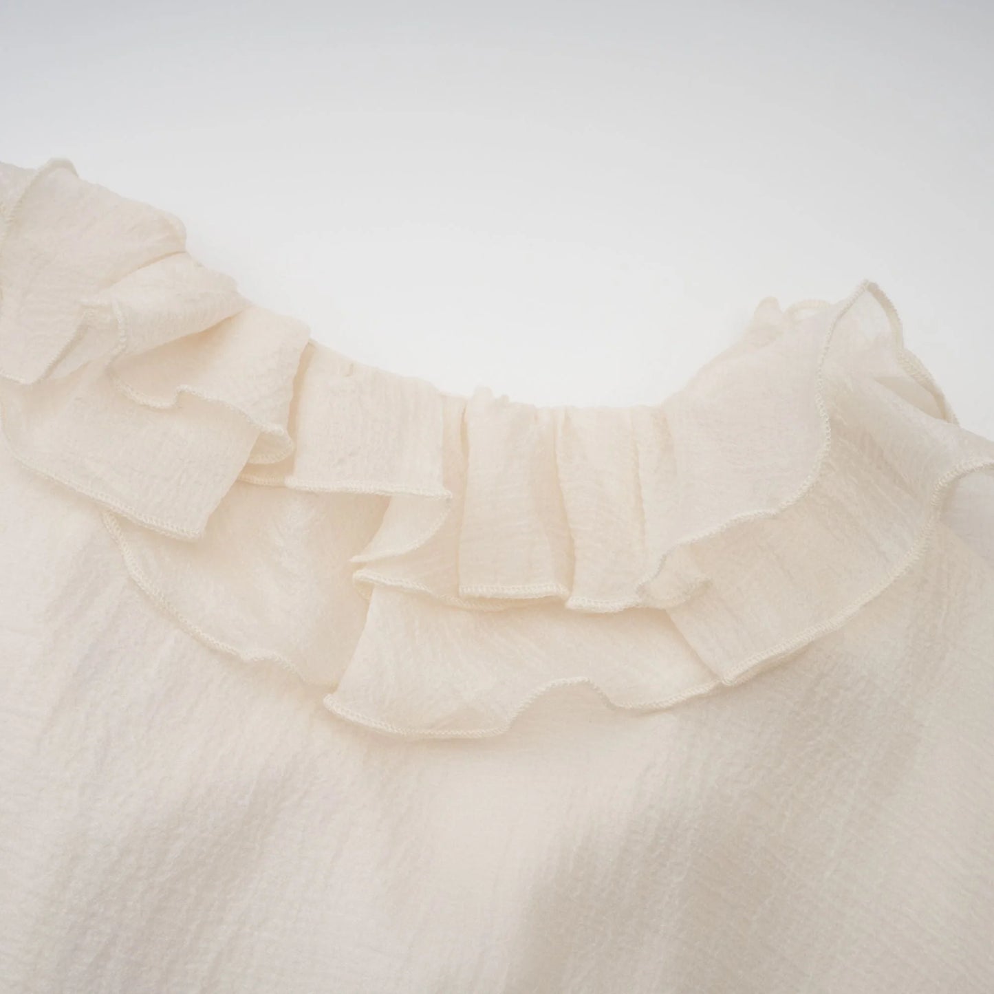 Close-up of a beige blouse with ruffled collar on a white background