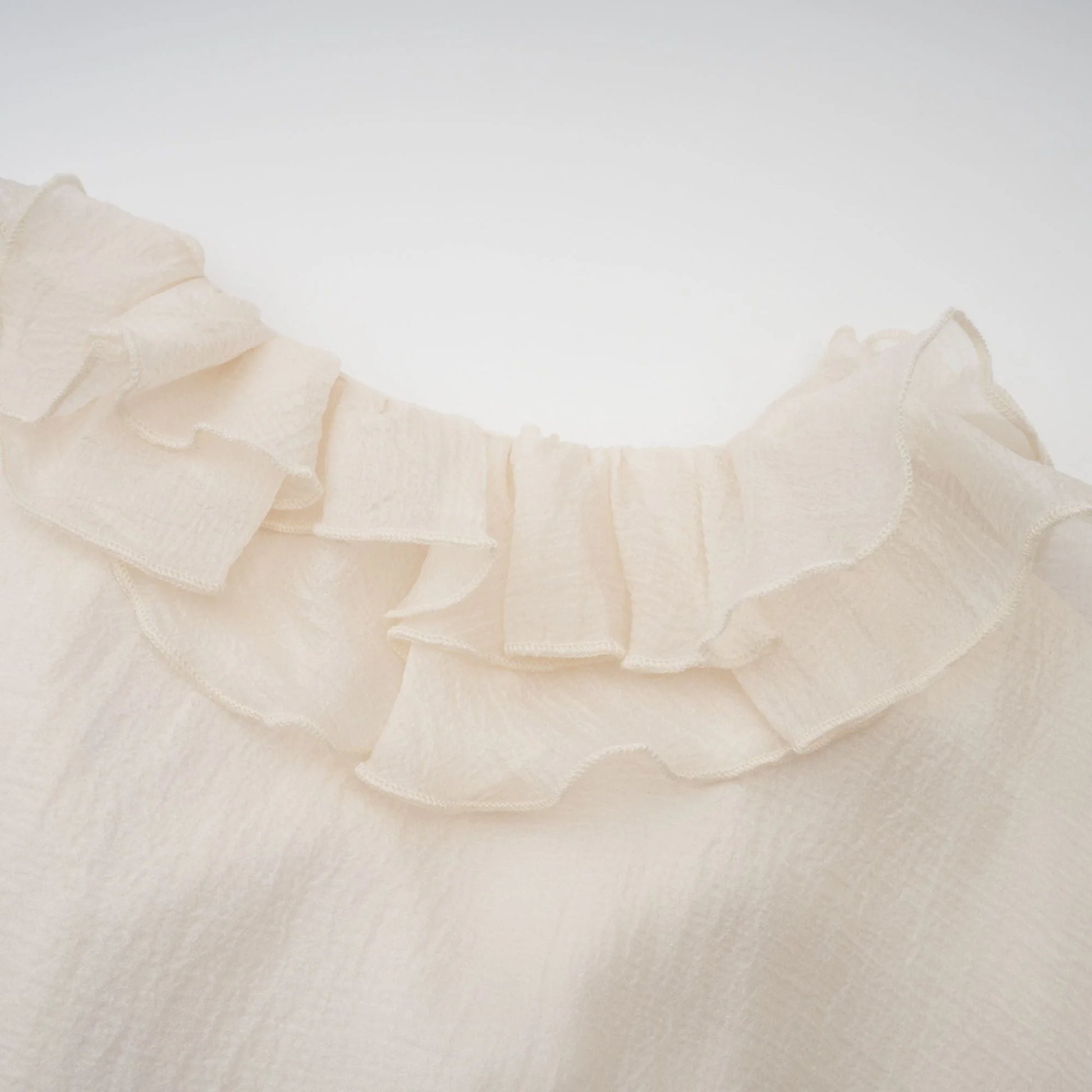 Close-up of a beige blouse with ruffled collar on a white background