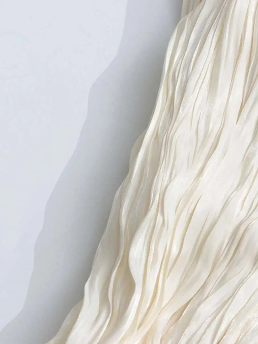 Close-up of a textured light beige dress with wavy ruffled patterns on a white background